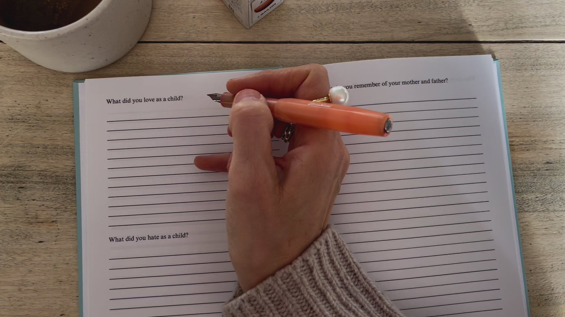 Load video: A hand holds a pen and writes in the journal answering the question, what did you love as a child?